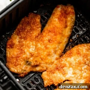 two cooked tilapia fillets arranged inside of a black air fryer basket.