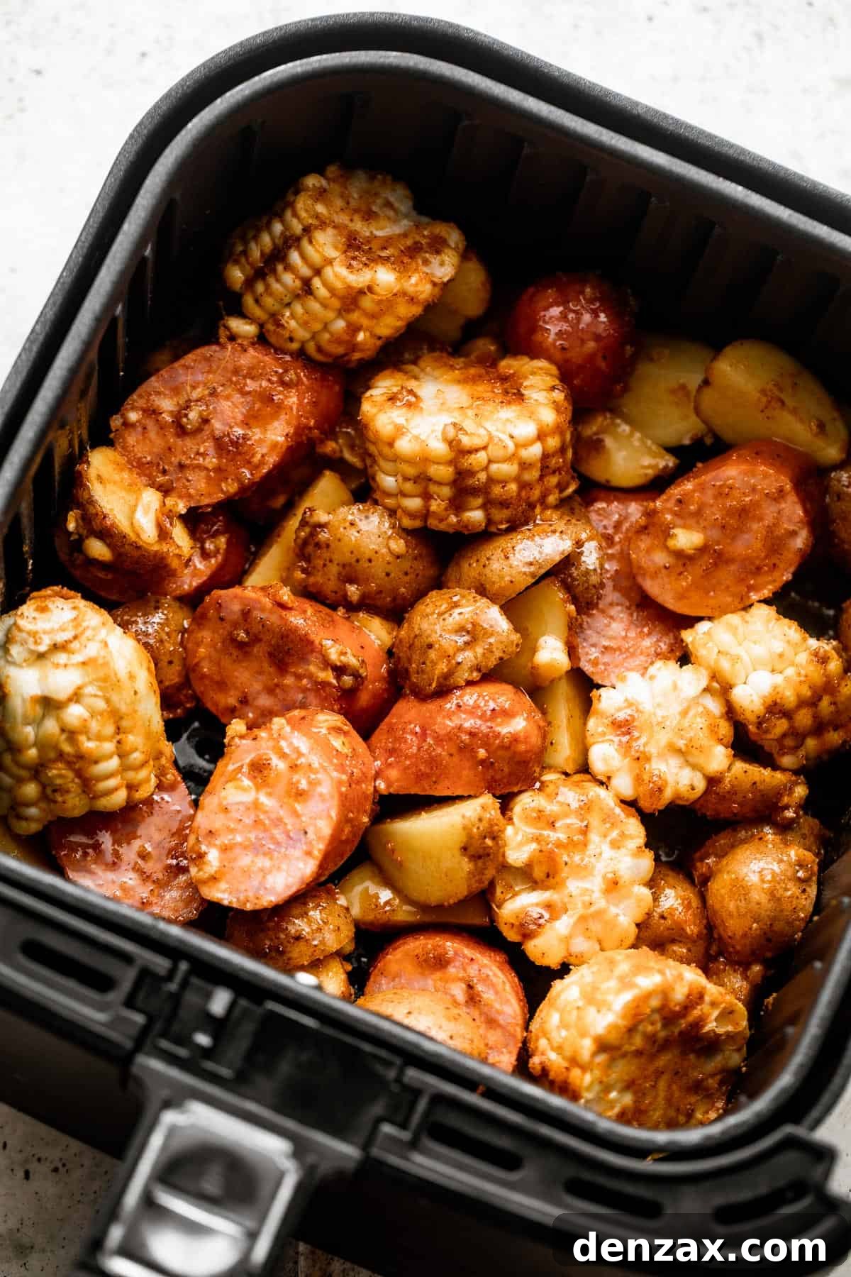 overhead shot of corn on the cob rounds, andouille sausage rounds, shrimp, and potatoes inside of a black air fryer basket.