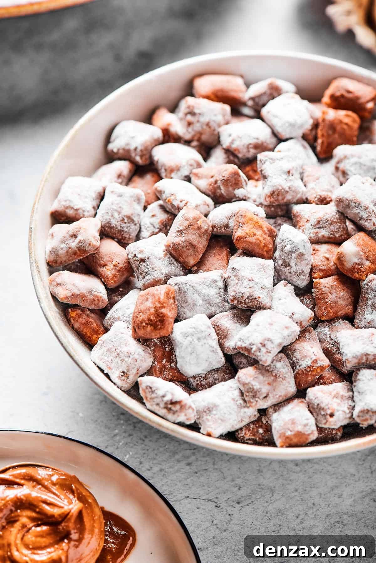 Close-up shot of puppy chow in a white bowl, to show the texture. Some pieces are fully coated in powdered sugar, while others are not.