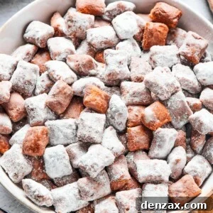 Close-up shot of puppy chow in a white bowl, to show the texture. Some pieces are fully coated in powdered sugar, while others are not.