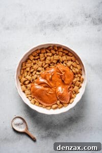 A large mixing bowl of Chex cereal, with a melted peanut butter chocolate mixture poured on top.