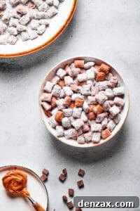 Muddy buddies in a white bowl, with a spoonful of peanut butter and a larger serving dish of the snack nearby.