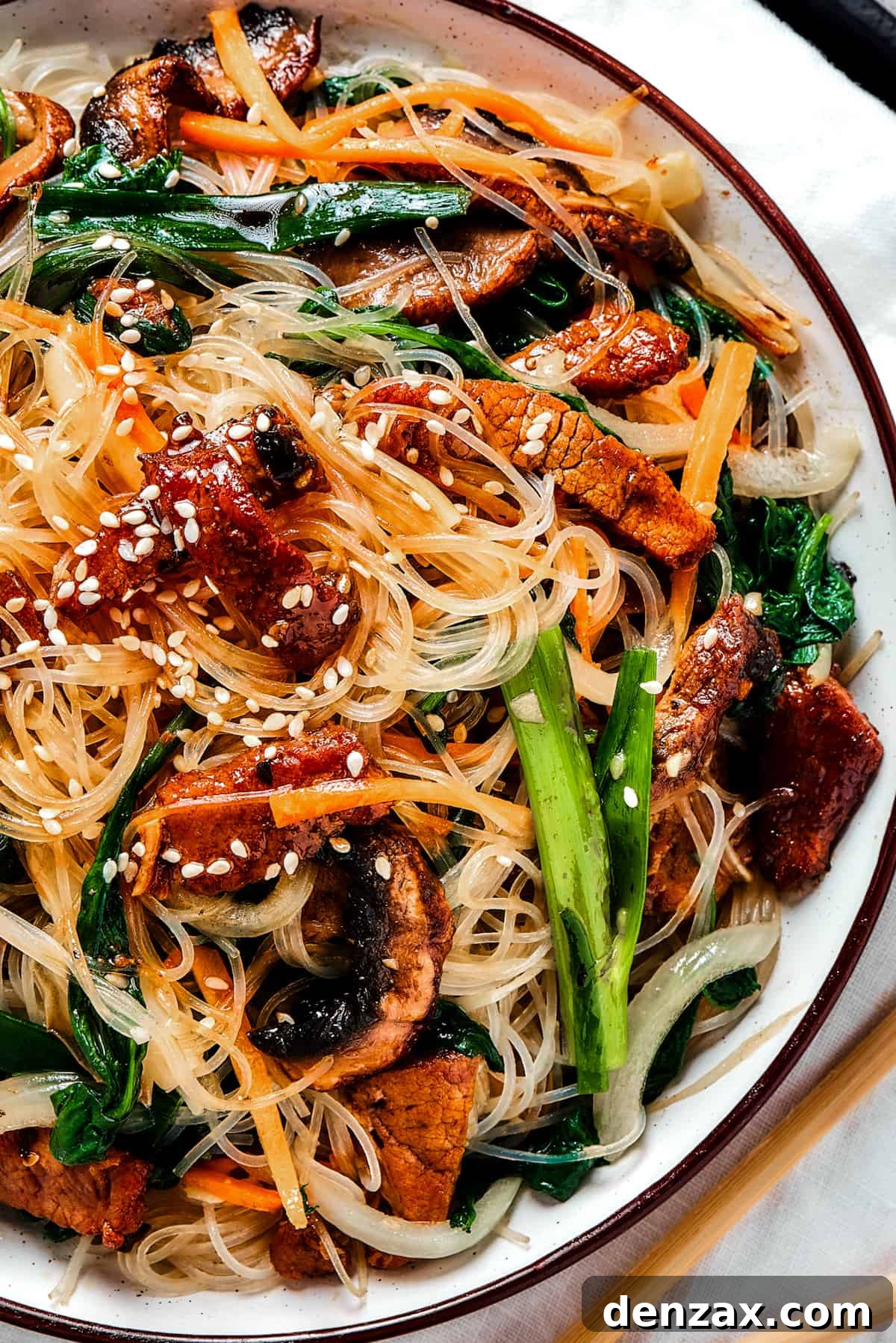 overhead shot of a shallow dish of beef noodle stir fry, garnished with sesame seeds.