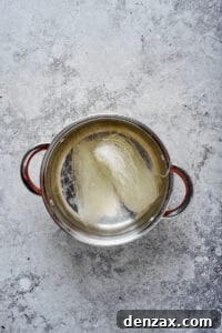 Glass noodles rehydrating in a stainless steel pot of hot water.