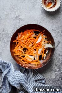 Matchstick carrots and sliced onions in a skillet.