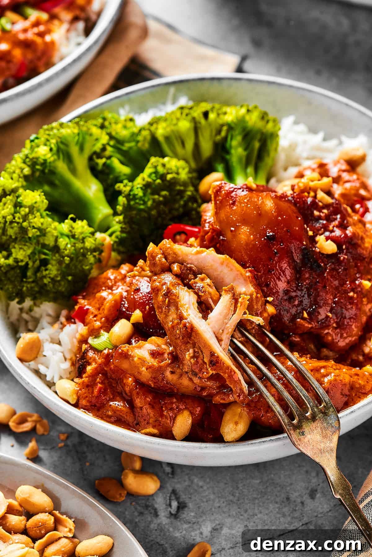 A close-up shot of a chicken thigh cooked in peanut sauce, with a fork pulling away a bite.