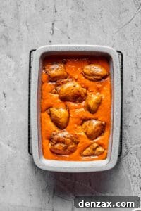 A baking dish full of creamy tomato peanut sauce, with chicken thighs arranged in the sauce.