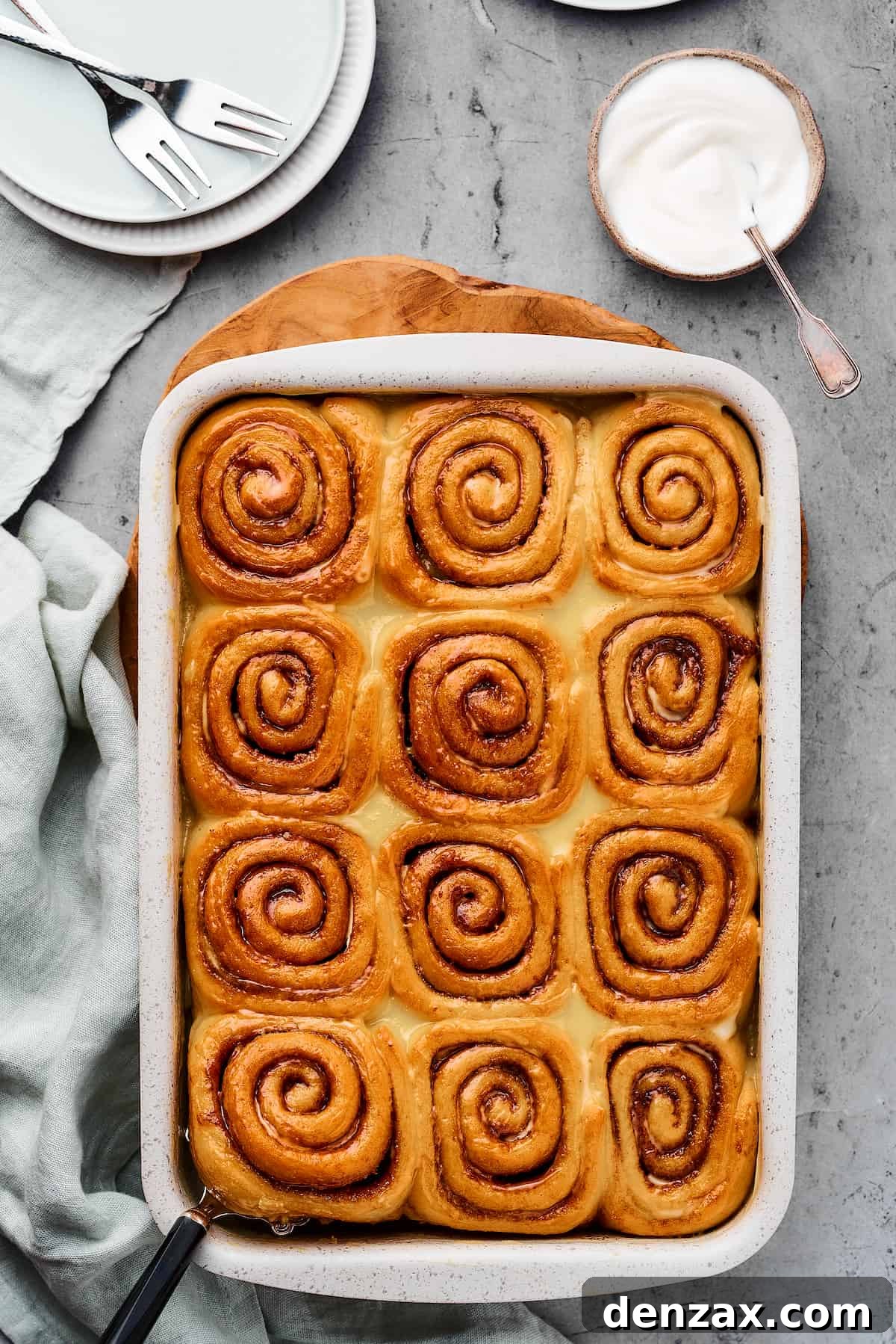 Homemade Cinnamon Rolls: Soft, Fluffy Recipe from Scratch 10 Baked cinnamon rolls in a baking pan, with a cloth dishtowel nearby.