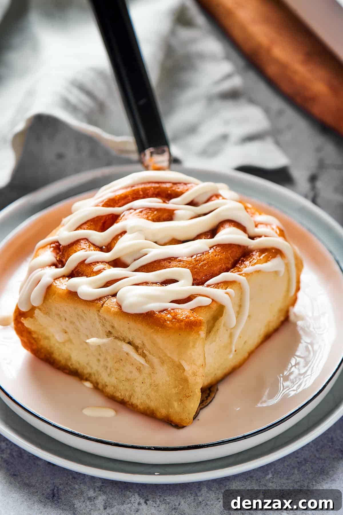 Homemade Cinnamon Rolls: Soft, Fluffy Recipe from Scratch 13 A fresh cinnamon bun on a small plate, with thick white glaze drizzled on top.