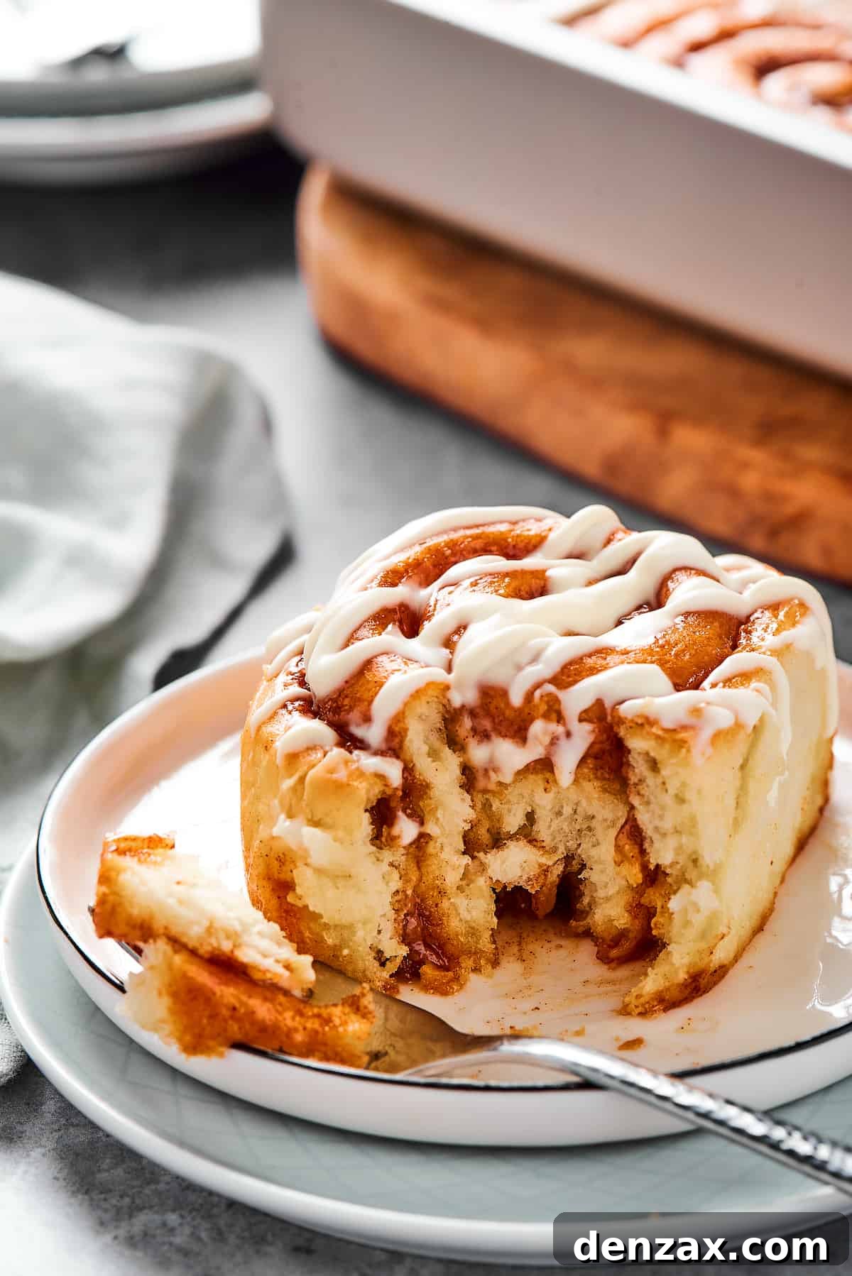 Soft, sticky Cinnamon Rolls from Scratch are simple to make and utterly addictive to eat! A bitten cinnamon bun on a small plate with a fork.