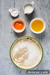 Homemade Cinnamon Rolls: Soft, Fluffy Recipe from Scratch 4 Dry baking ingredients mixed in a large mixing bowl. Sugar, milk, egg yolks, and melted butter are near the bowl in separate dishes.