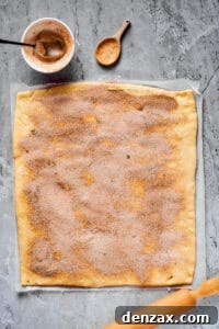Homemade Cinnamon Rolls: Soft, Fluffy Recipe from Scratch 7 A work surface with a large rectangle of dough, a rolling pin, and a small bowl of cinnamon sugar nearby. Cinnamon sugar has been sprinkled generously all over the dough.