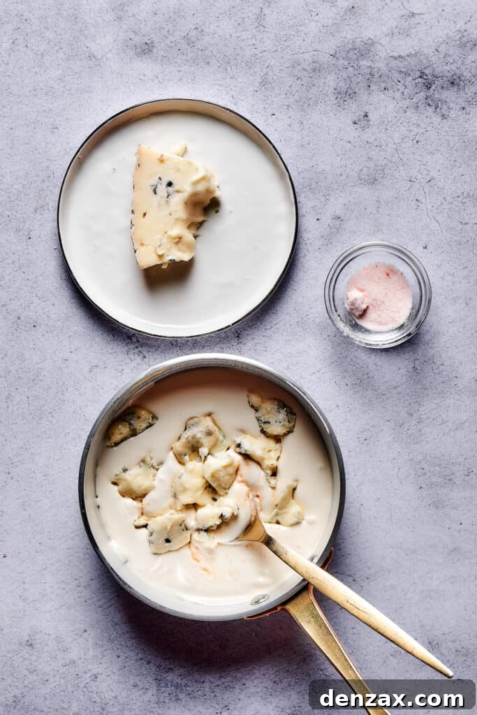 Chunks of blue cheese being stirred into a saucepan of creamy sauce.