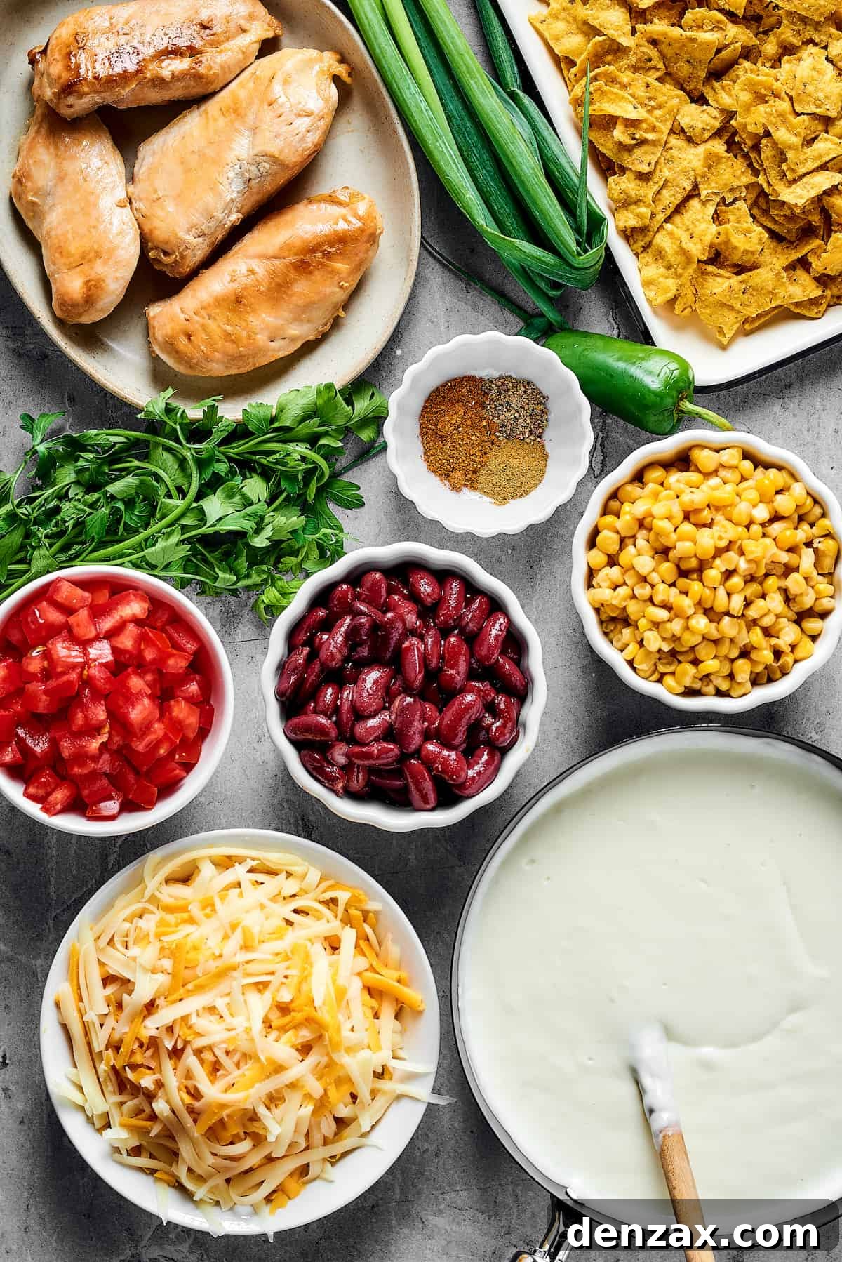 From top: Cooked chicken breast, green onions, crushed chips, seasonings, chopped tomatoes, beans, corn, cheese, white sauce.