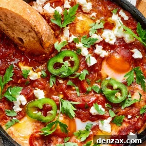 A slice of toasted bread dipped in chunky tomato sauce and poached eggs, garnished with jalapeno and feta cheese.