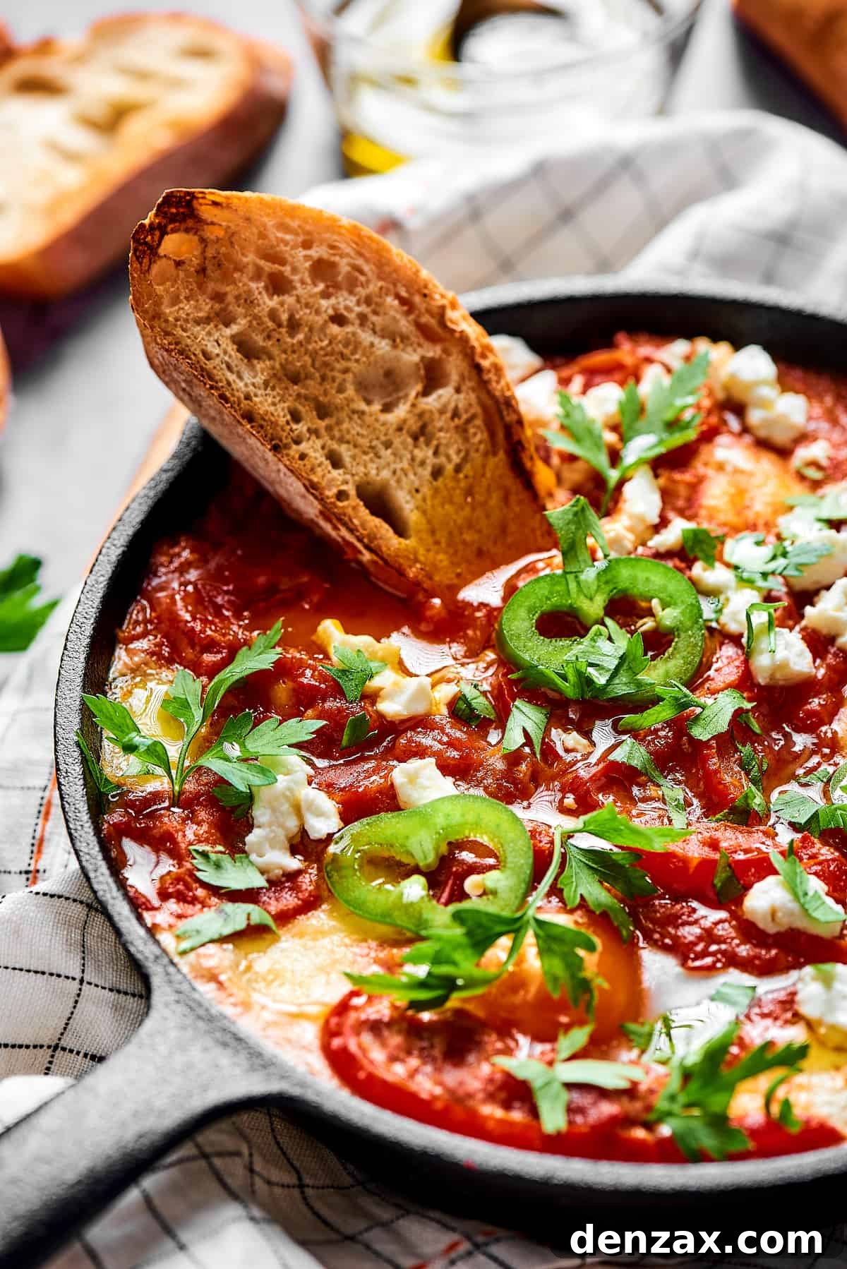 A slice of toasted bread dipped in chunky tomato sauce and poached eggs, garnished with jalapeno and feta cheese.