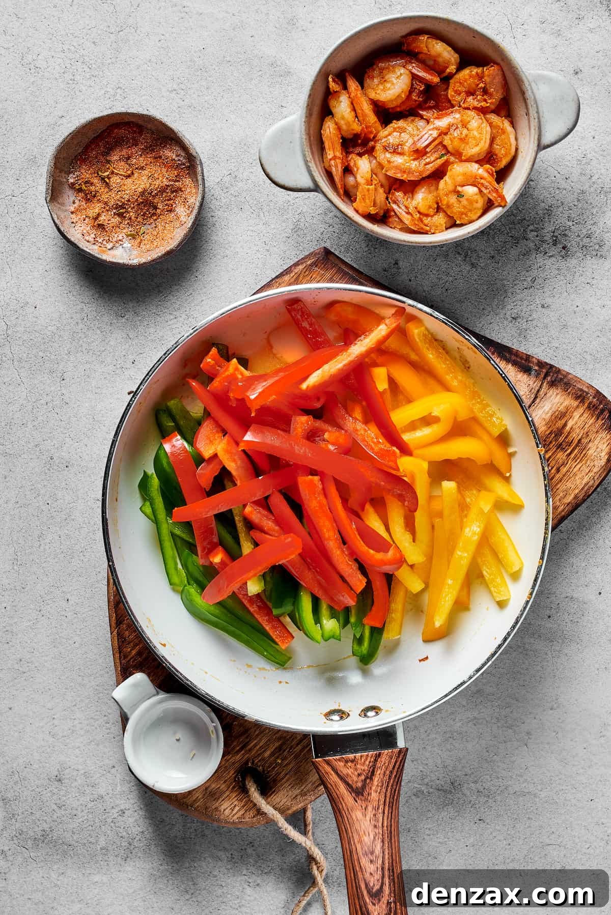 Green, red, and yellow bell peppers in a skillet, next to a bowl of spicy shrimp.