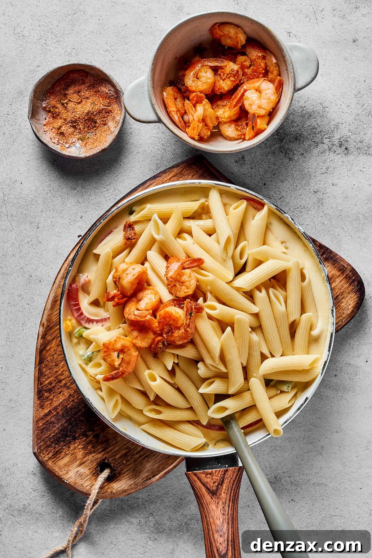 Shrimp and pasta being mixed into a skillet of sauce.
