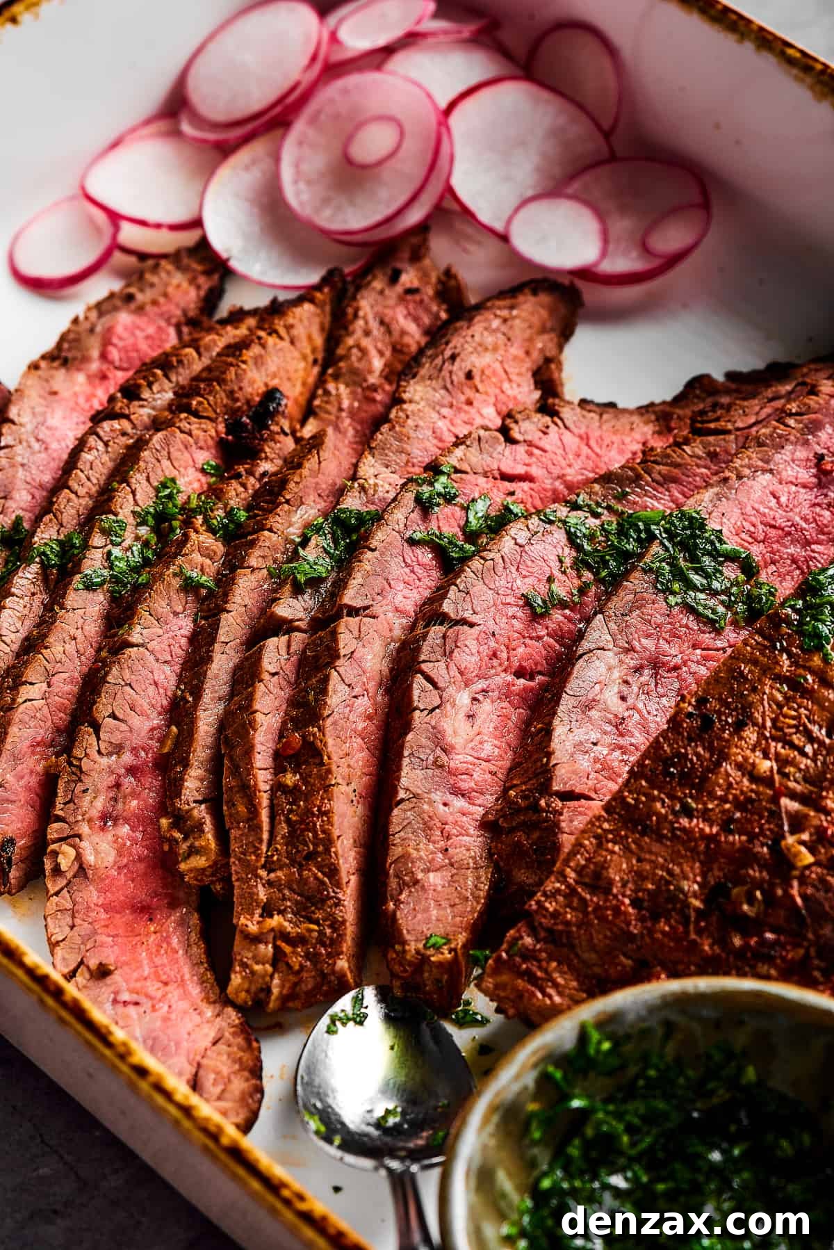 Slices of steak next to a cup of herb sauce.