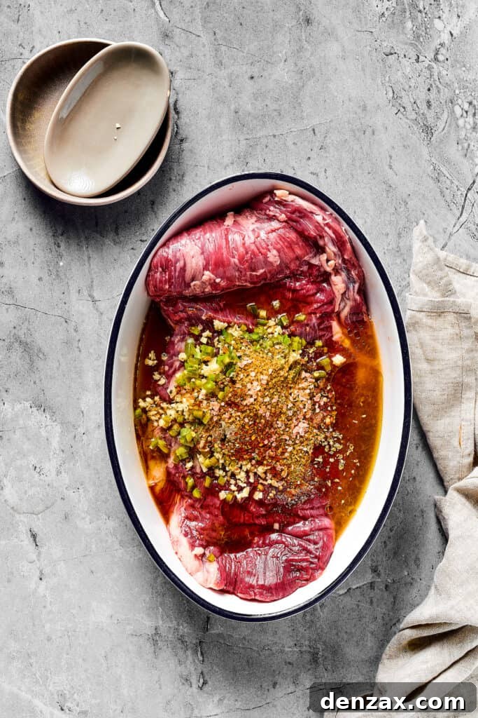 A flank steak in an enamel oval dish, covered in marinade.