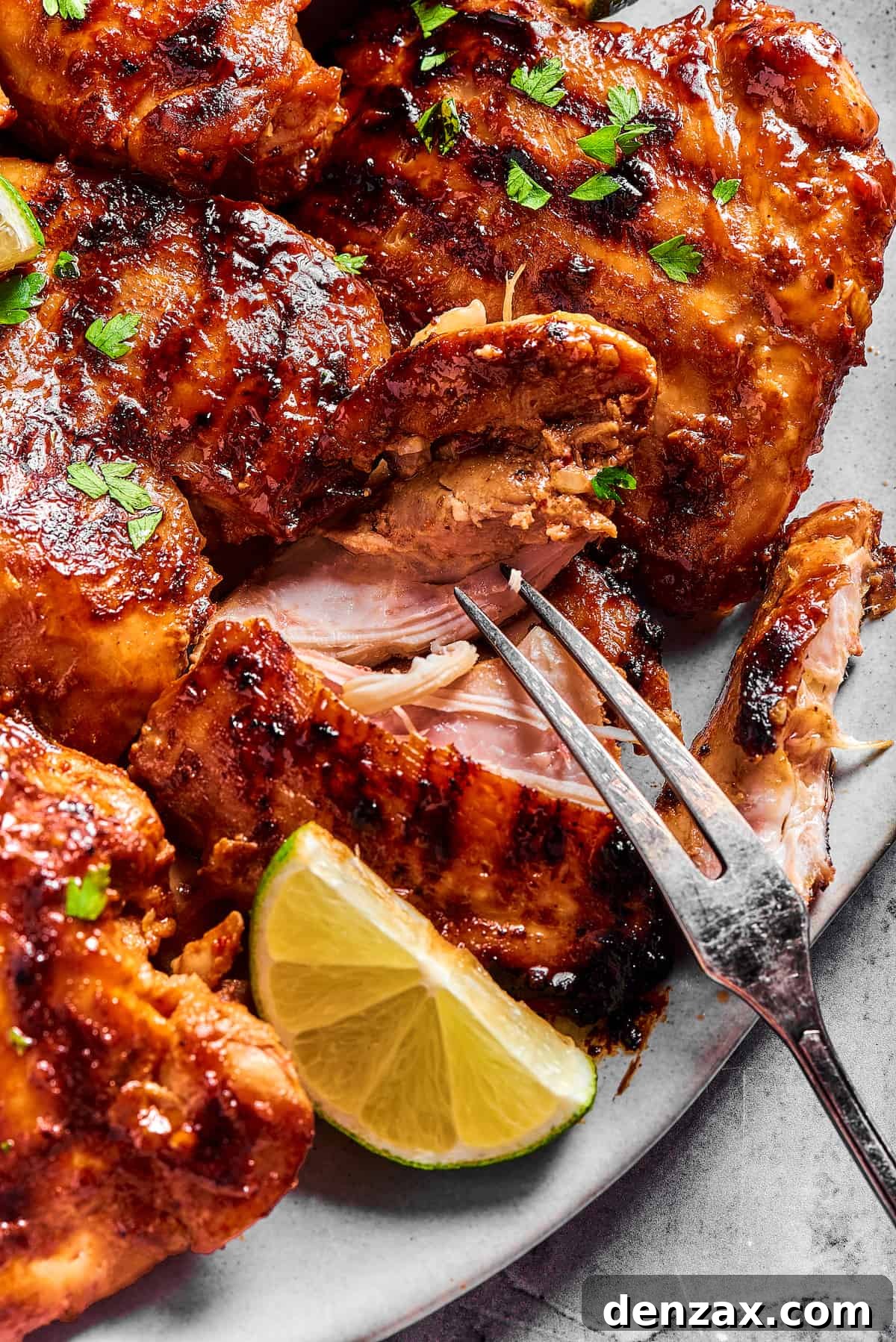 A platter of grilled chicken, with one piece being pulled apart by a grilling fork to show the texture of the interior.