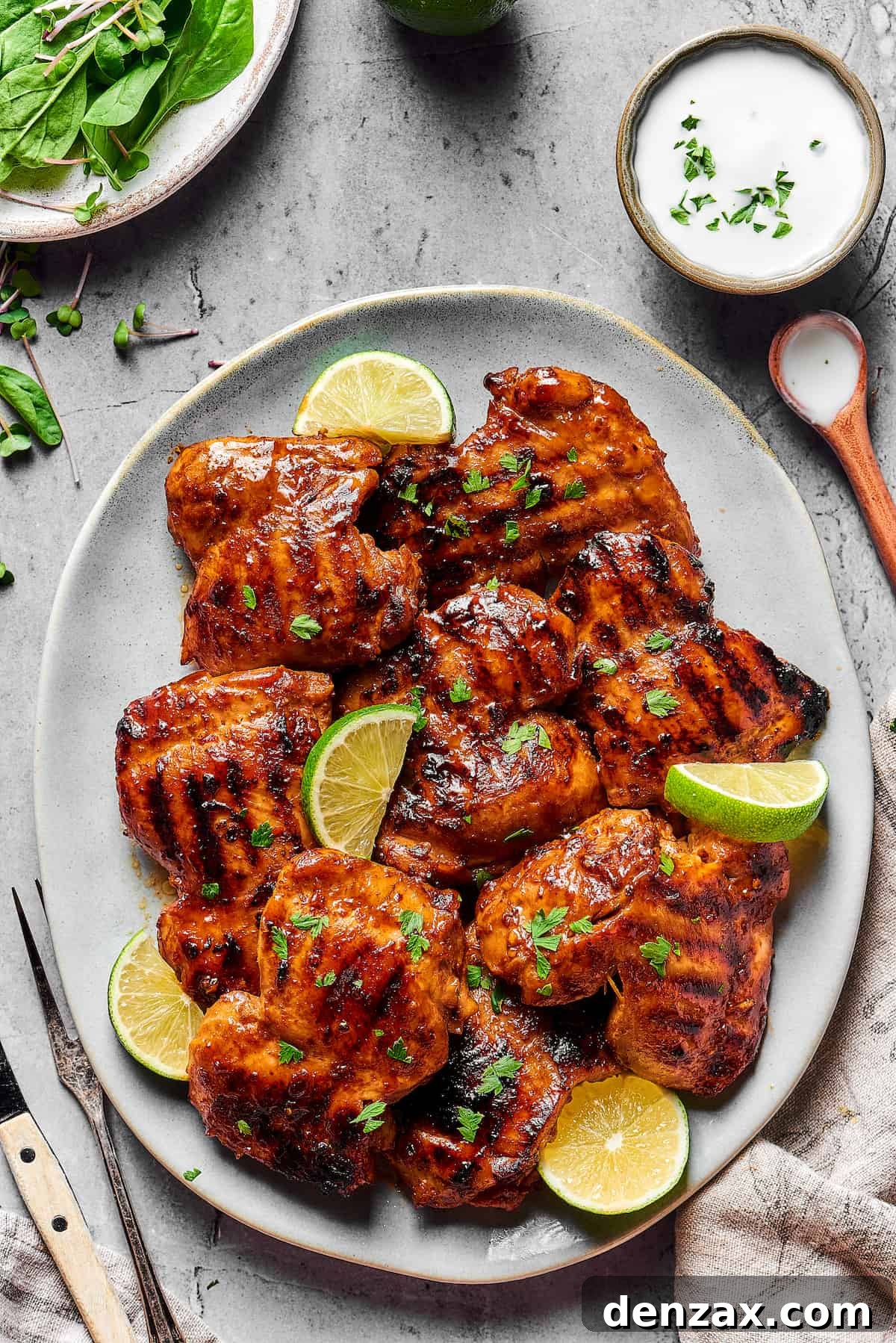 An oval platter of grilled chicken thighs, garnished with parsley and lime wedges.