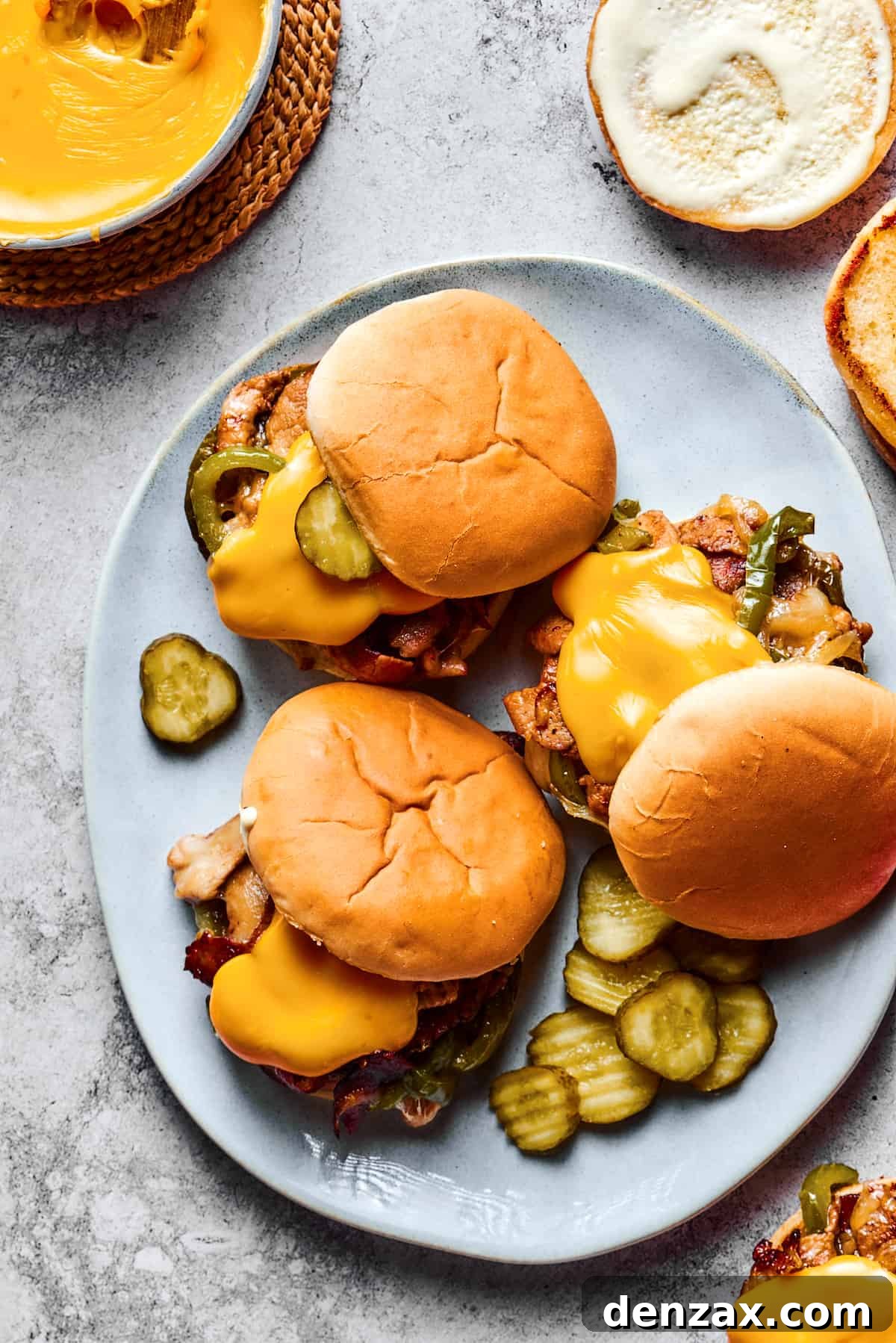 Overhead shot of a large platter. Three sandwiches are on the platter, each one piled high with philly cheesesteak fillings and garnished with pickles.