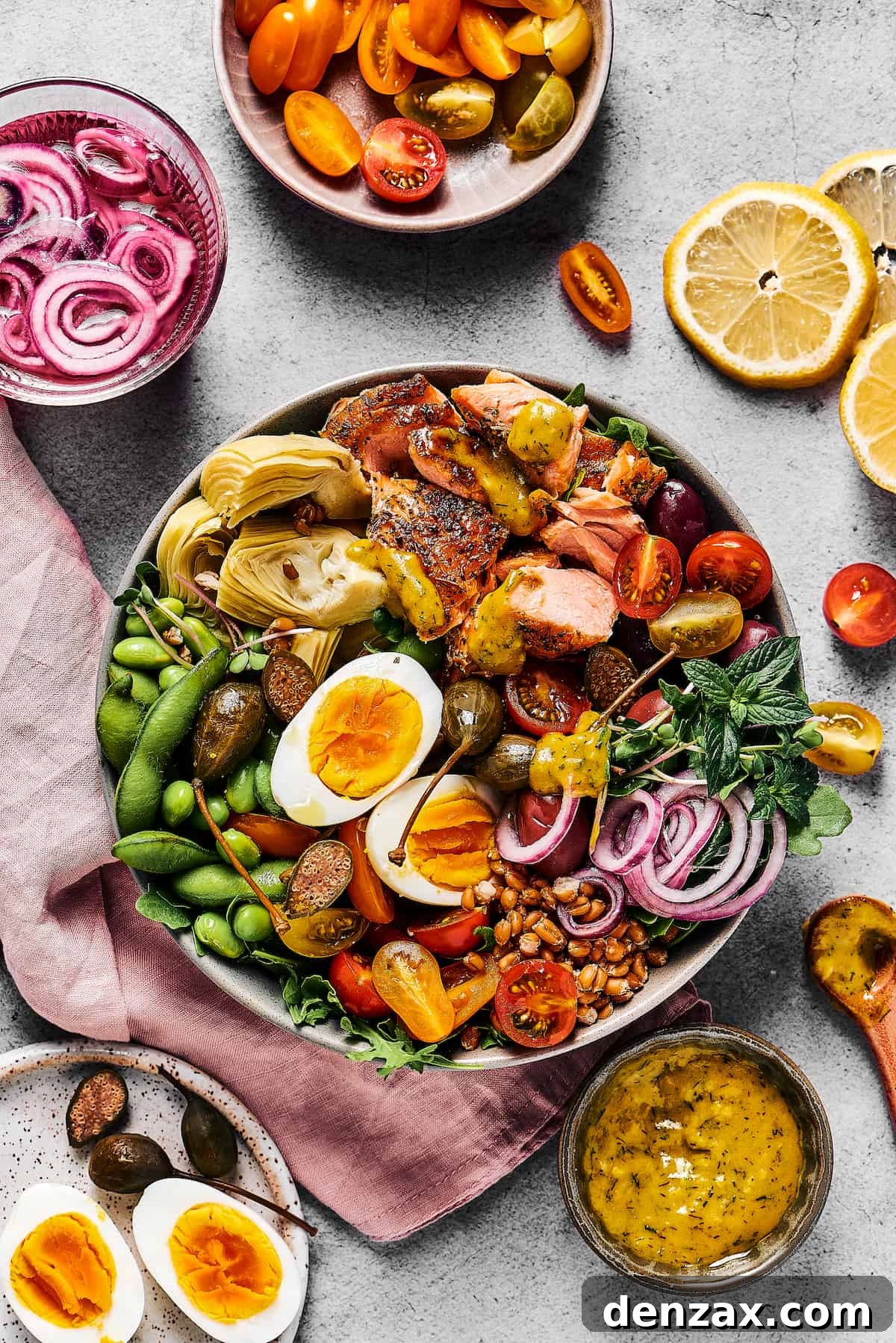 A large salad with lots of ingredients, in a bowl. Dishes of ingredients are arranged nearby on the table.