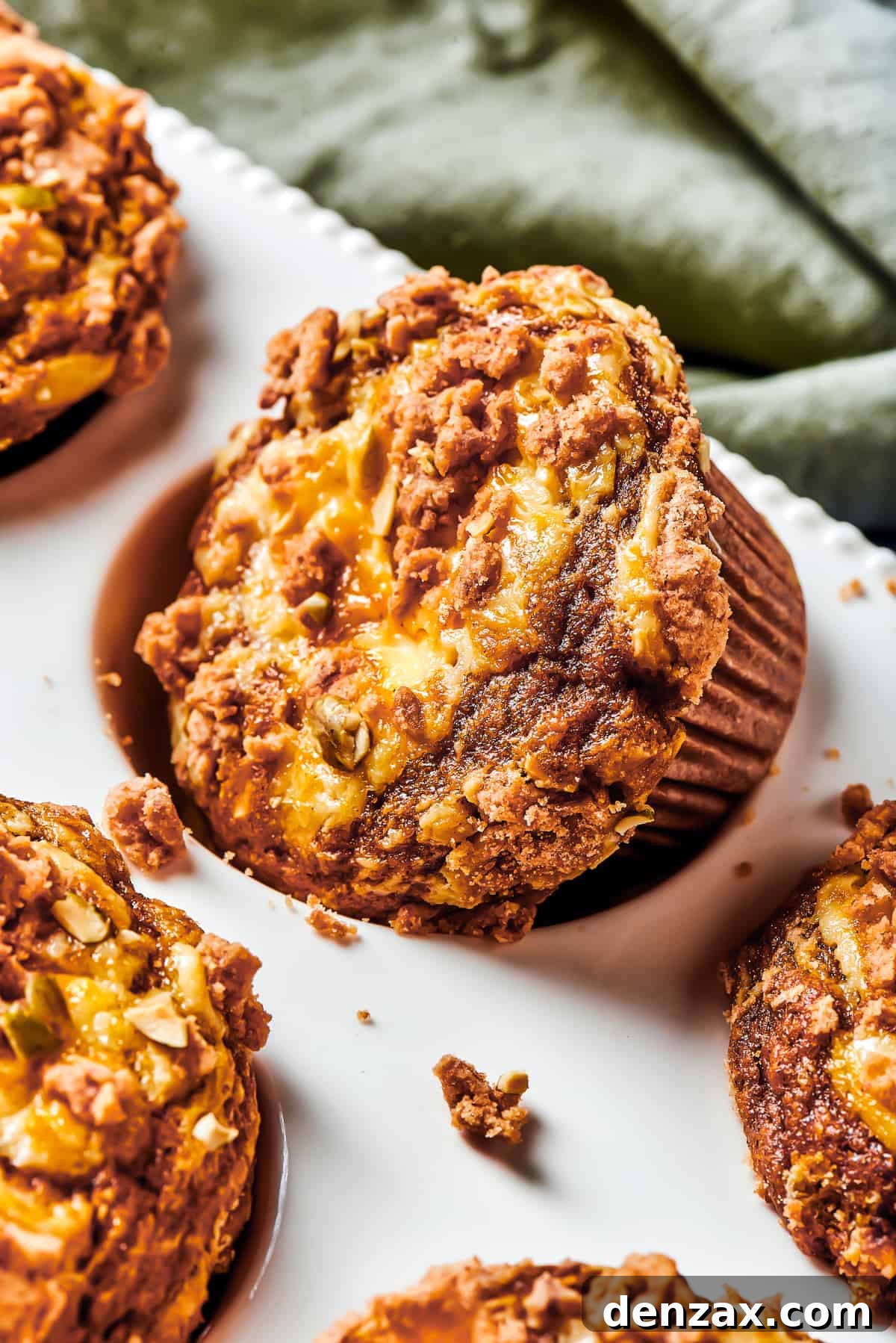 A muffin tin with one muffin turned diagonally in its well. Small pieces of topping have fallen off onto the muffin tin.