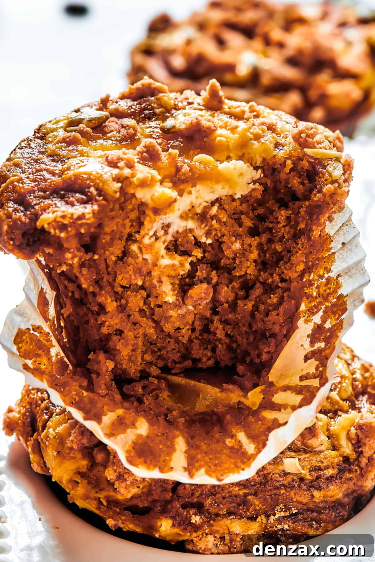 A pumpkin muffin broken in half with the paper muffin cup peeled away.