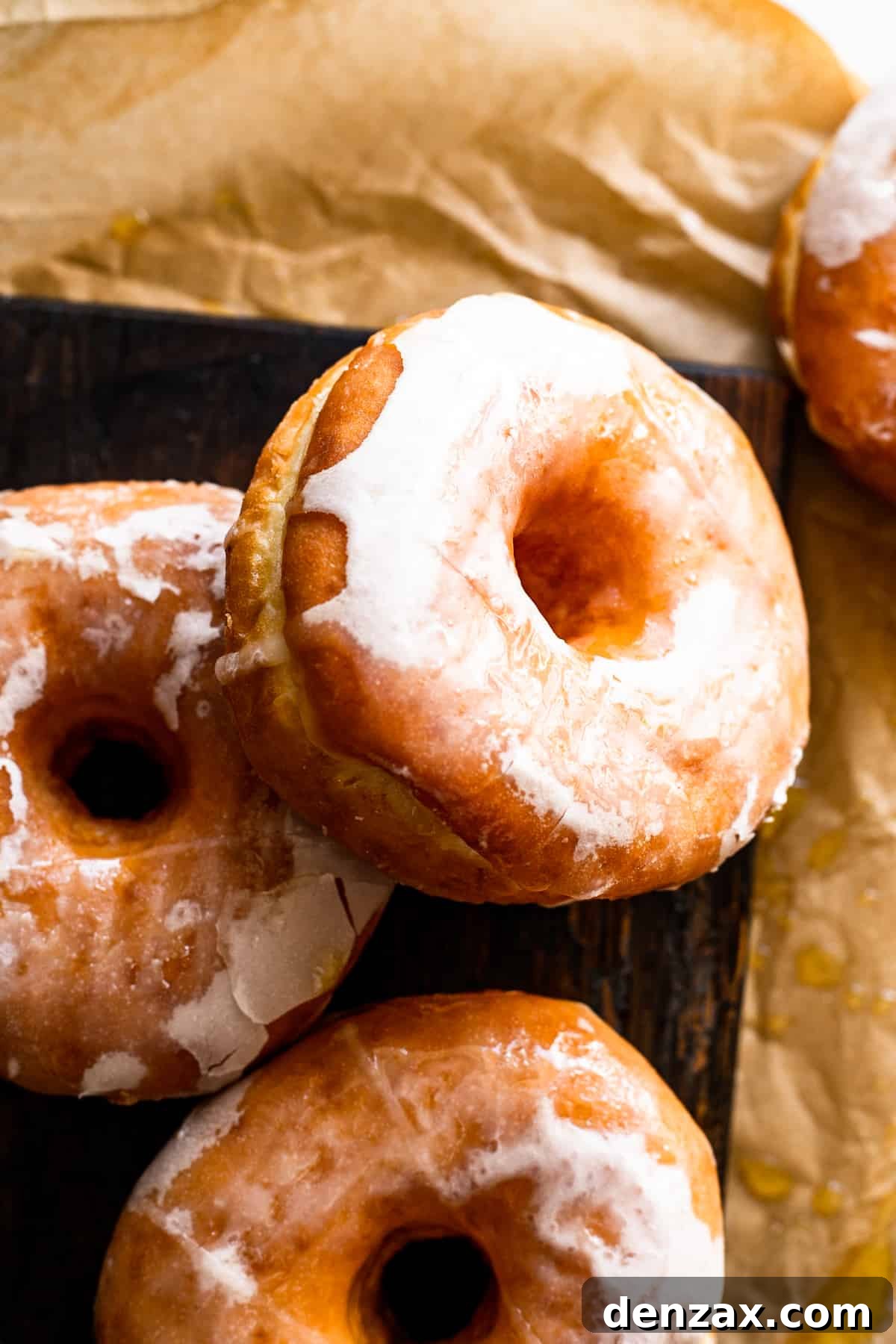 Maple-Glazed Baked Apple Cider Doughnuts for Fall Treats 3 apple cider maple glazed doughnuts resting on a wooden board.