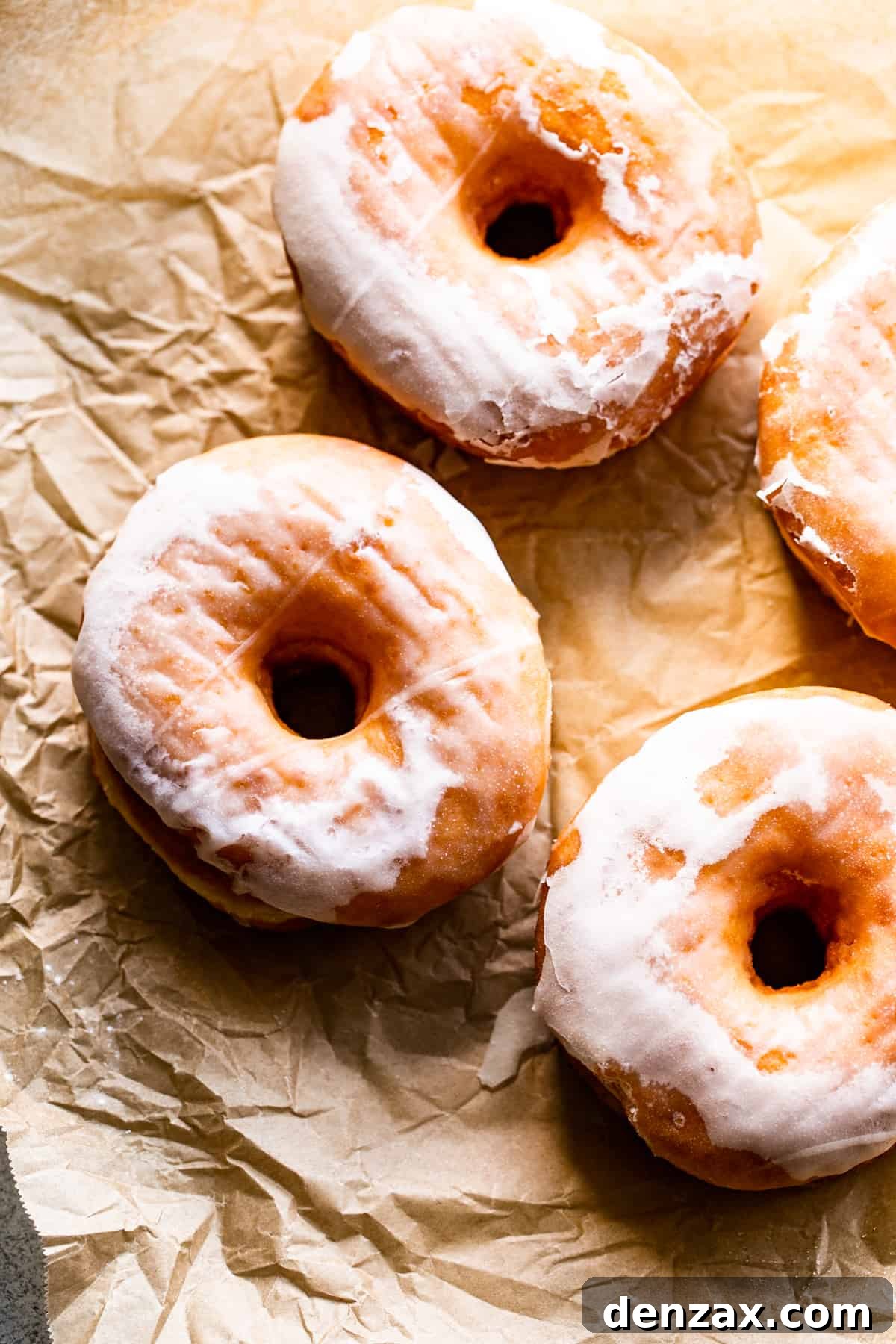 Maple-Glazed Baked Apple Cider Doughnuts for Fall Treats 4 three glazed donuts arranged on top of a light brown baking paper.