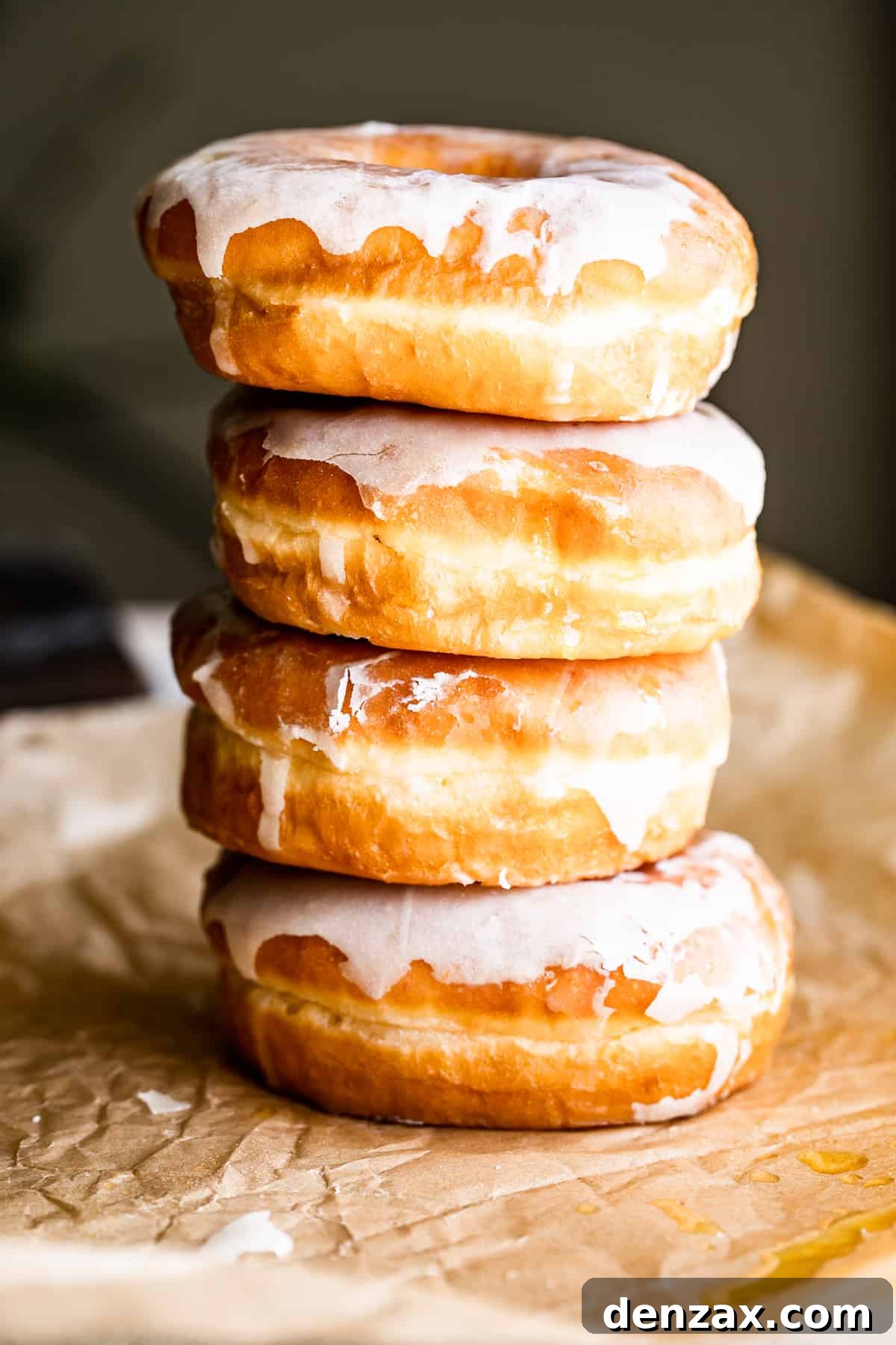 Maple-Glazed Baked Apple Cider Doughnuts for Fall Treats 5 four apple cider doughnuts stacked one on top of the other, and pictured against a brown backdrop.