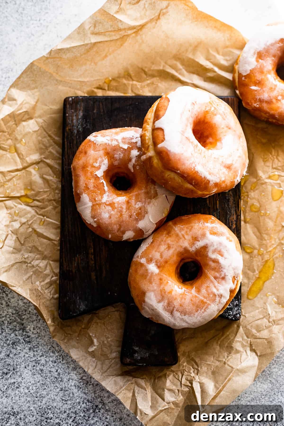 Maple-Glazed Baked Apple Cider Doughnuts for Fall Treats 6 overhead photo of three doughnuts arranged on a dark brown wooden board with a donut set to the side in the upper right hand corner.