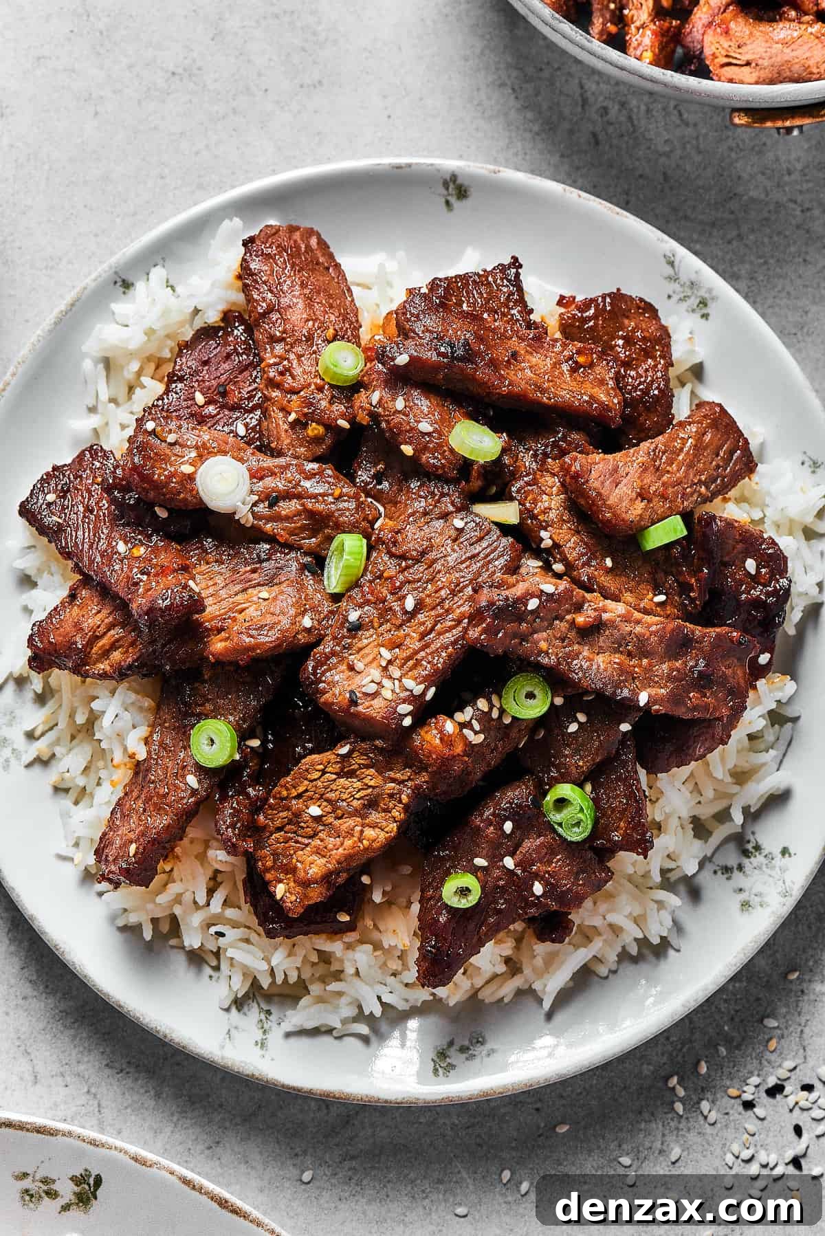 Beef bulgogi served onto a white plate, over a bed of rice.