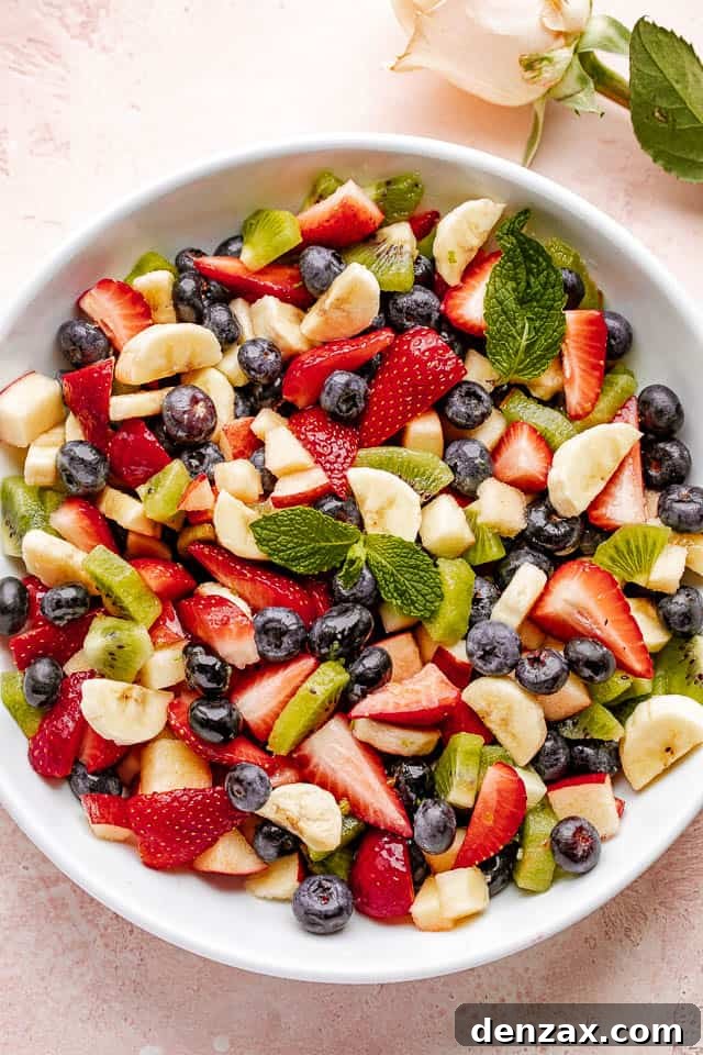 Fresh fruit salad in a large white bowl garnished with fresh mint leaves.