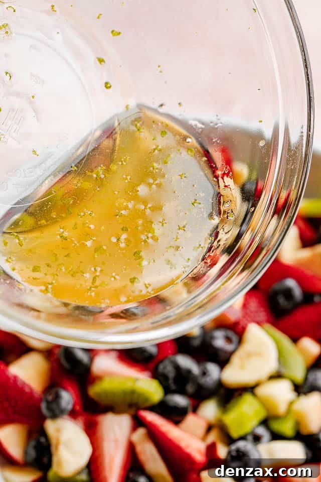 The honey lime dressing being poured on the fruit salad.
