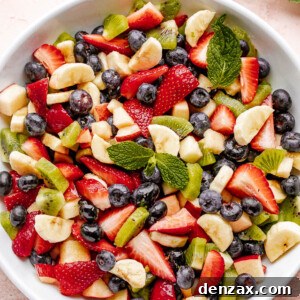 Fresh fruit salad in a large white bowl garnished with fresh mint leaves.