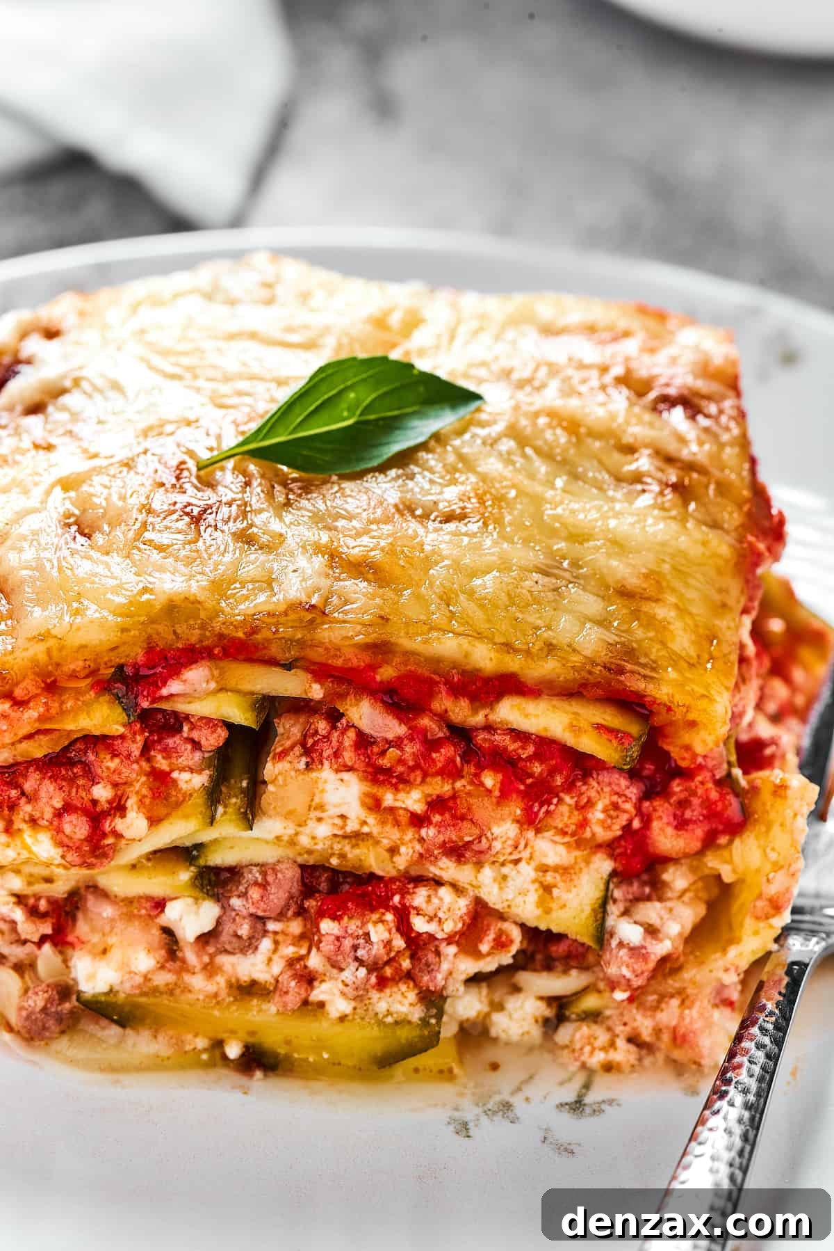 A serving of lasagna on a white plate with a fork.
