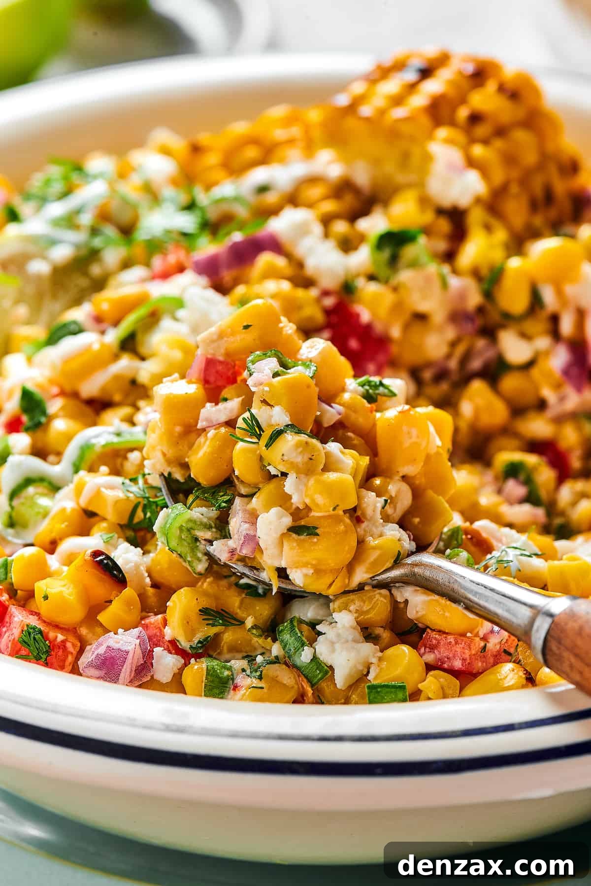 A spoonful of grilled corn salad being lifted toward the camera from a serving dish.