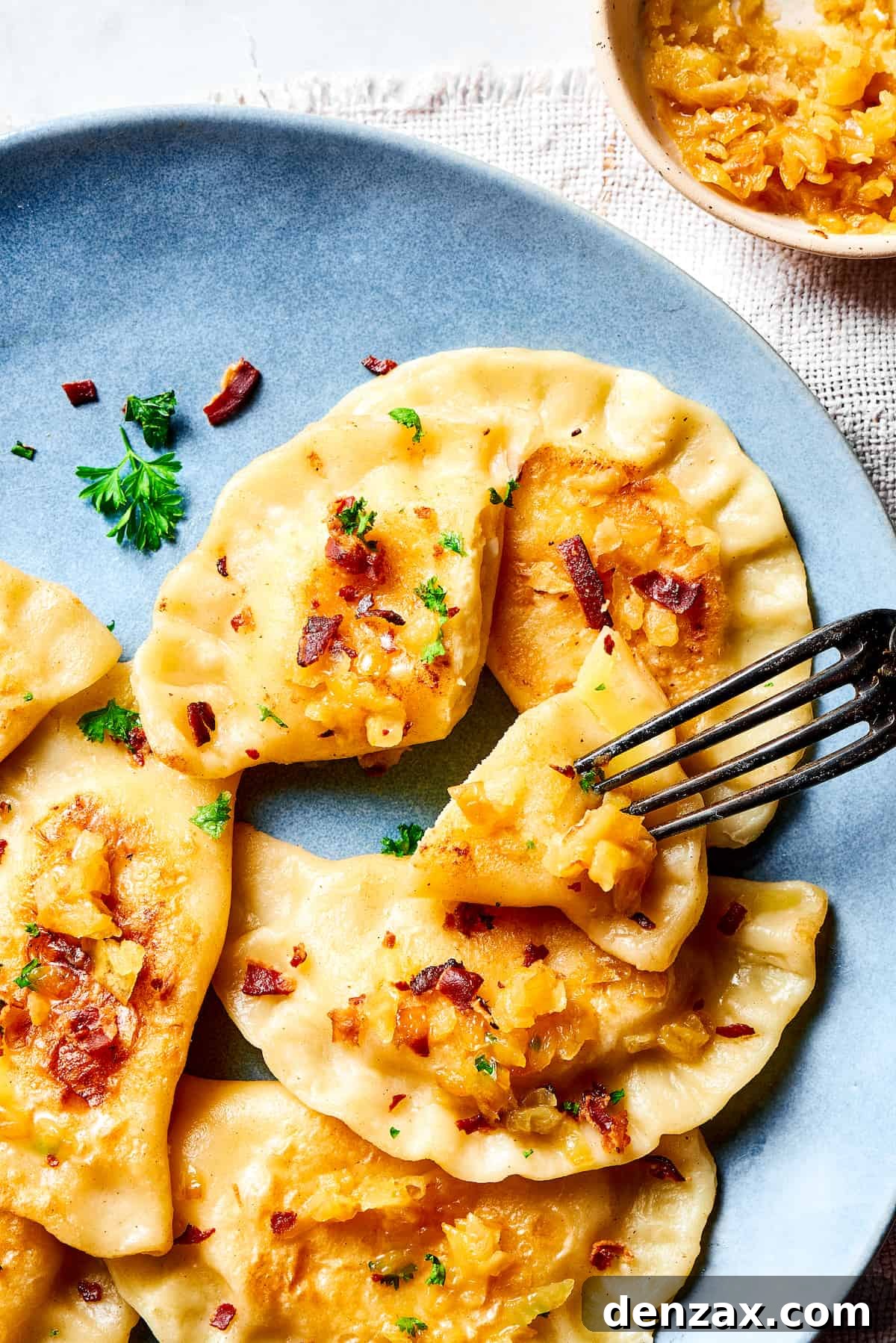 A fork piercing a bite-sized piece of a pierogi.