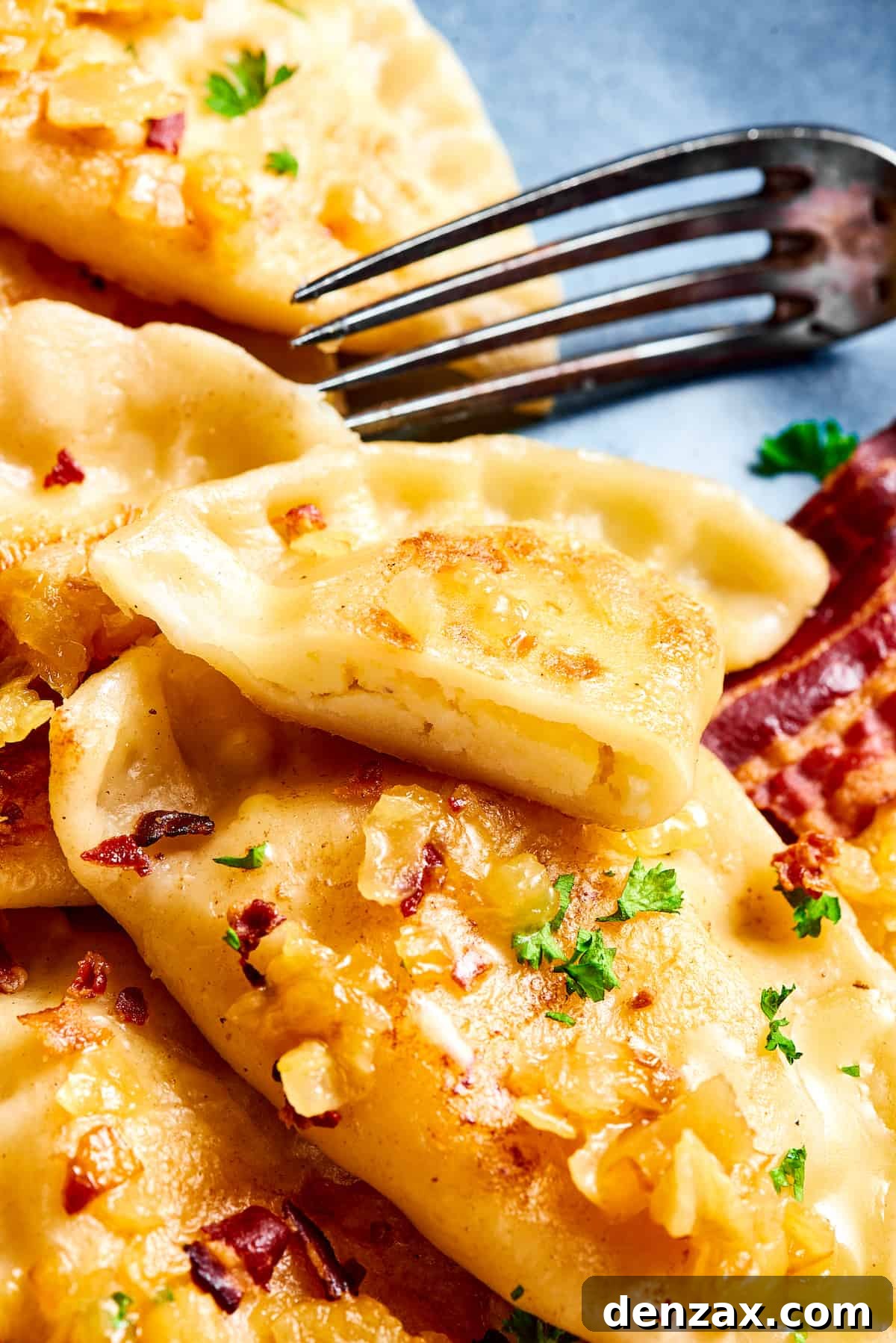 A plate of pierogies. One has been cut in half with a fork.