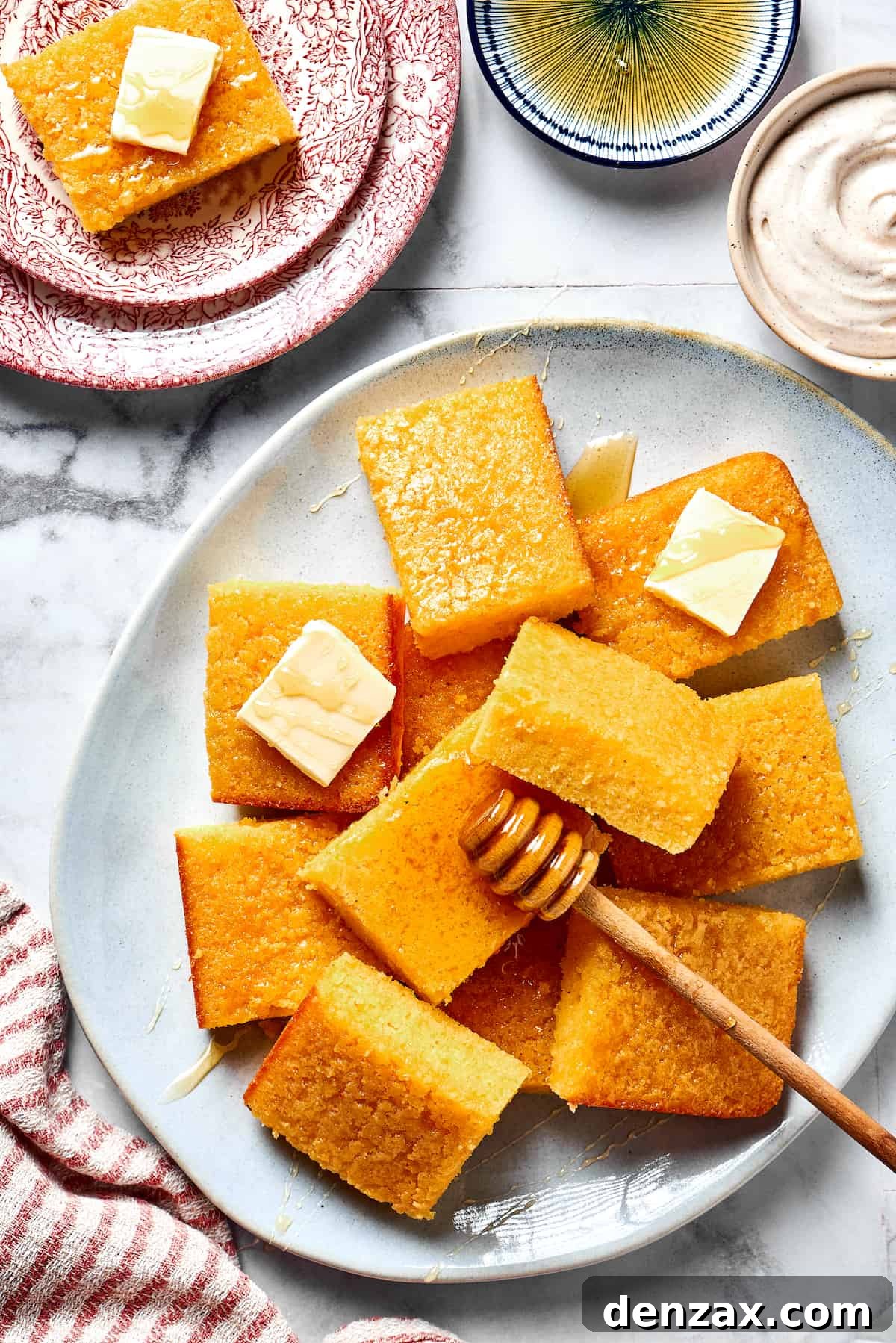 Squares of cornbread on a plate with pats of butter and a small honey dipper.