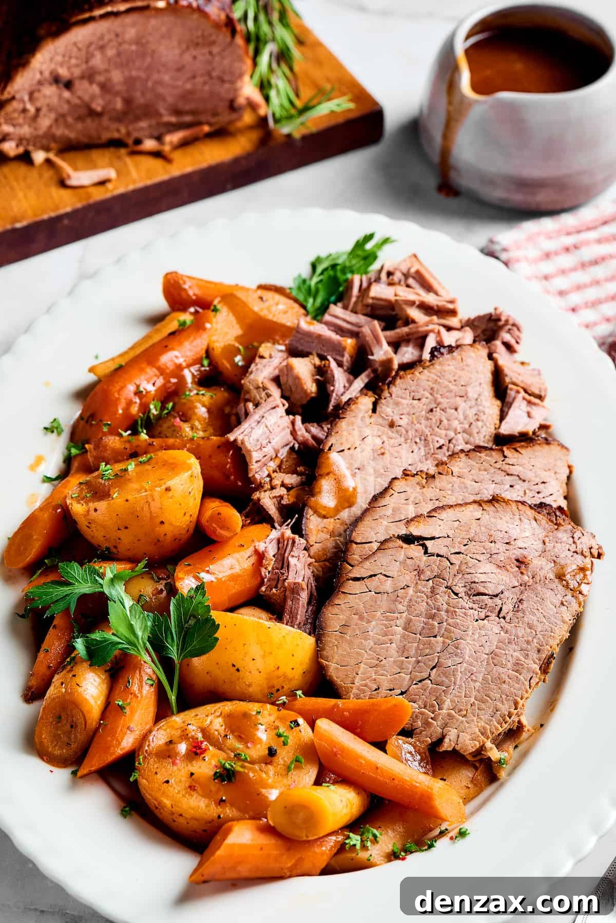 A platter of pot roast with vegetables next to a carving board with roast beef, and a pitcher of gravy.