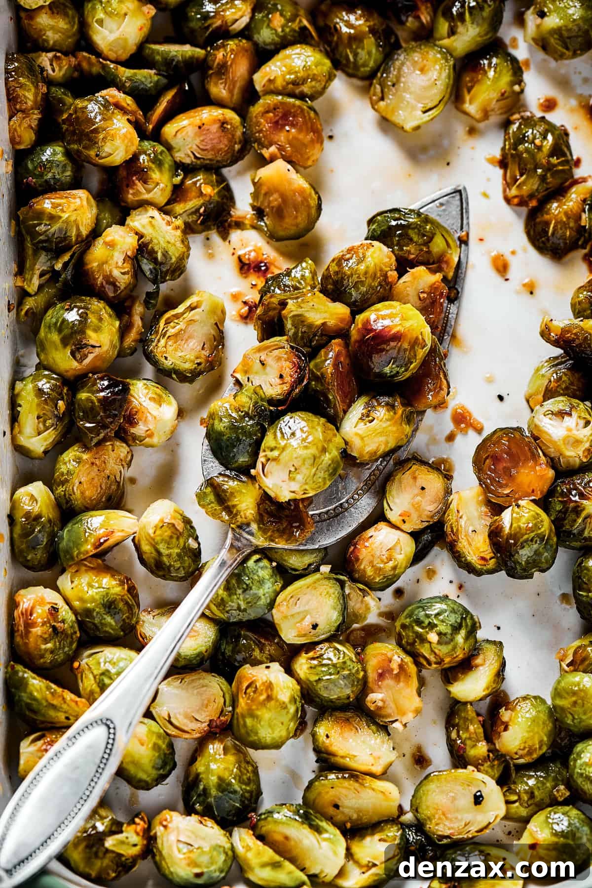 These Roasted Brussel Sprouts are oven-roasted with garlic and drizzled with a killer maple-pomegranate glaze. A veggie side you’ll crave! Tossing roasted brussels sprouts with glaze.