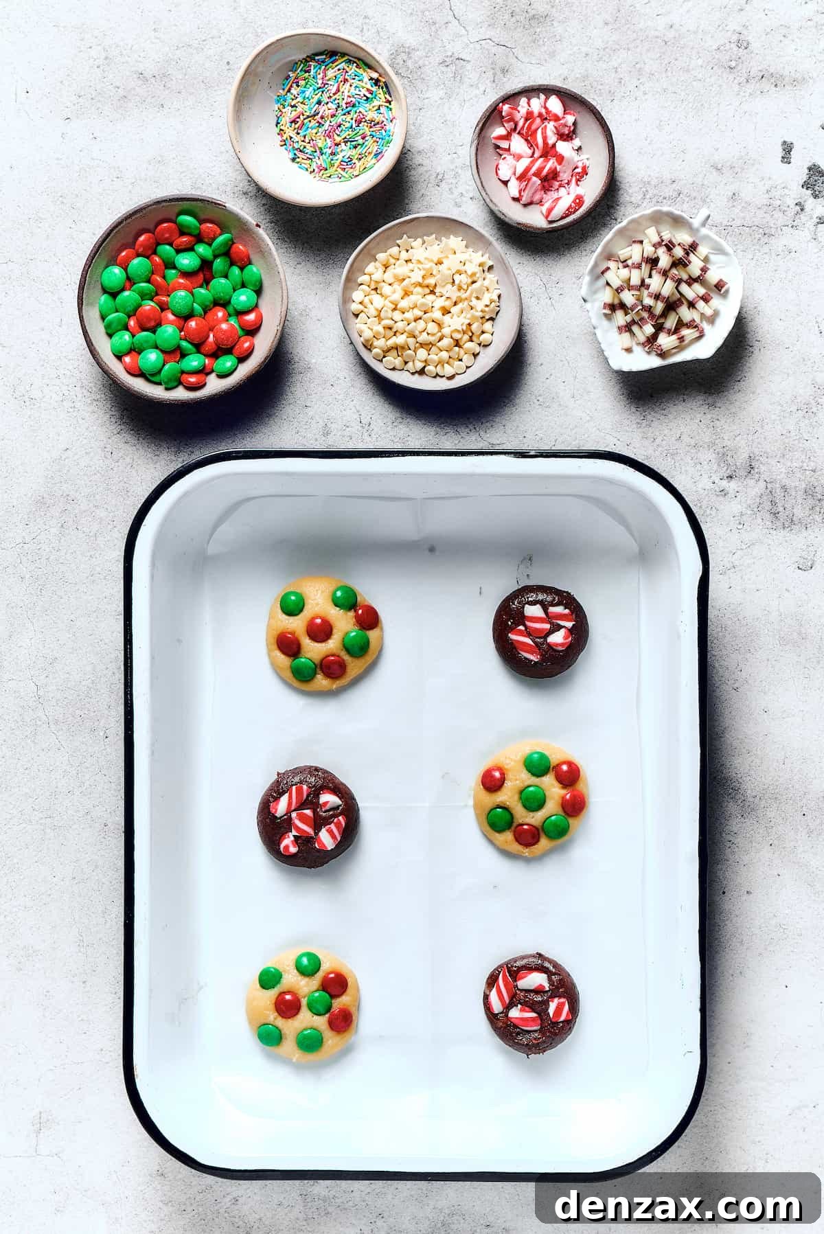 Unbaked chocolate and vanilla cookies on a baking sheet, with M&M's pressed into the dough.