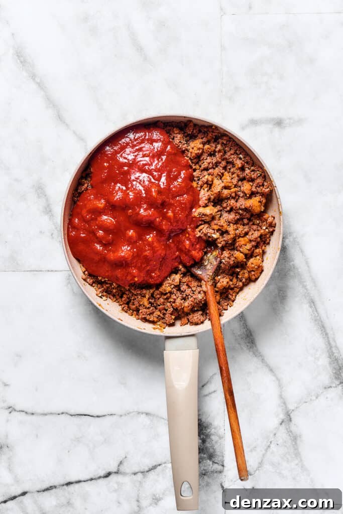 Crushed tomatoes added to meat sauce in a skillet.