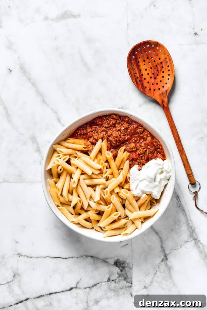 Mostaccioli pasta, ricotta, and meat sauce in a mixing bowl.