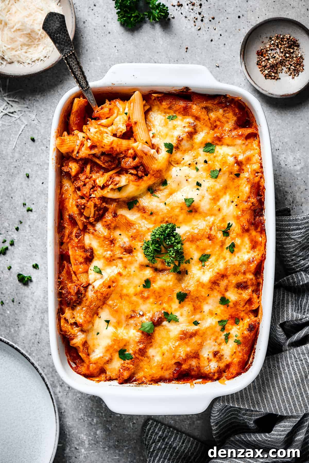 overhead shot Scooping out a spoonful of baked mostaccioli from a large baking dish.