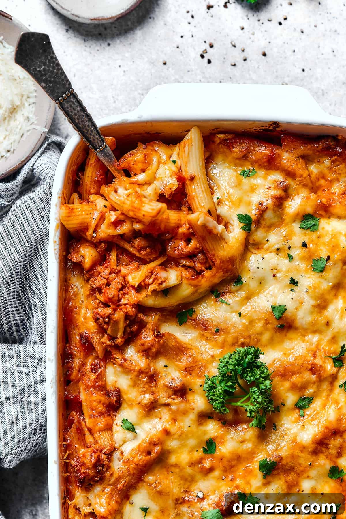 Scooping out a spoonful of baked mostaccioli from a large baking dish.